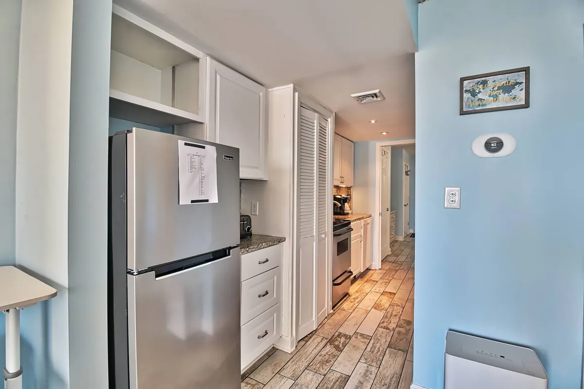 The shot captures a modern kitchen with stainless steel appliances, white cabinets, and warm wooden floors. The space is open and functional, perfect for groups to prepare meals or snacks before a night out.