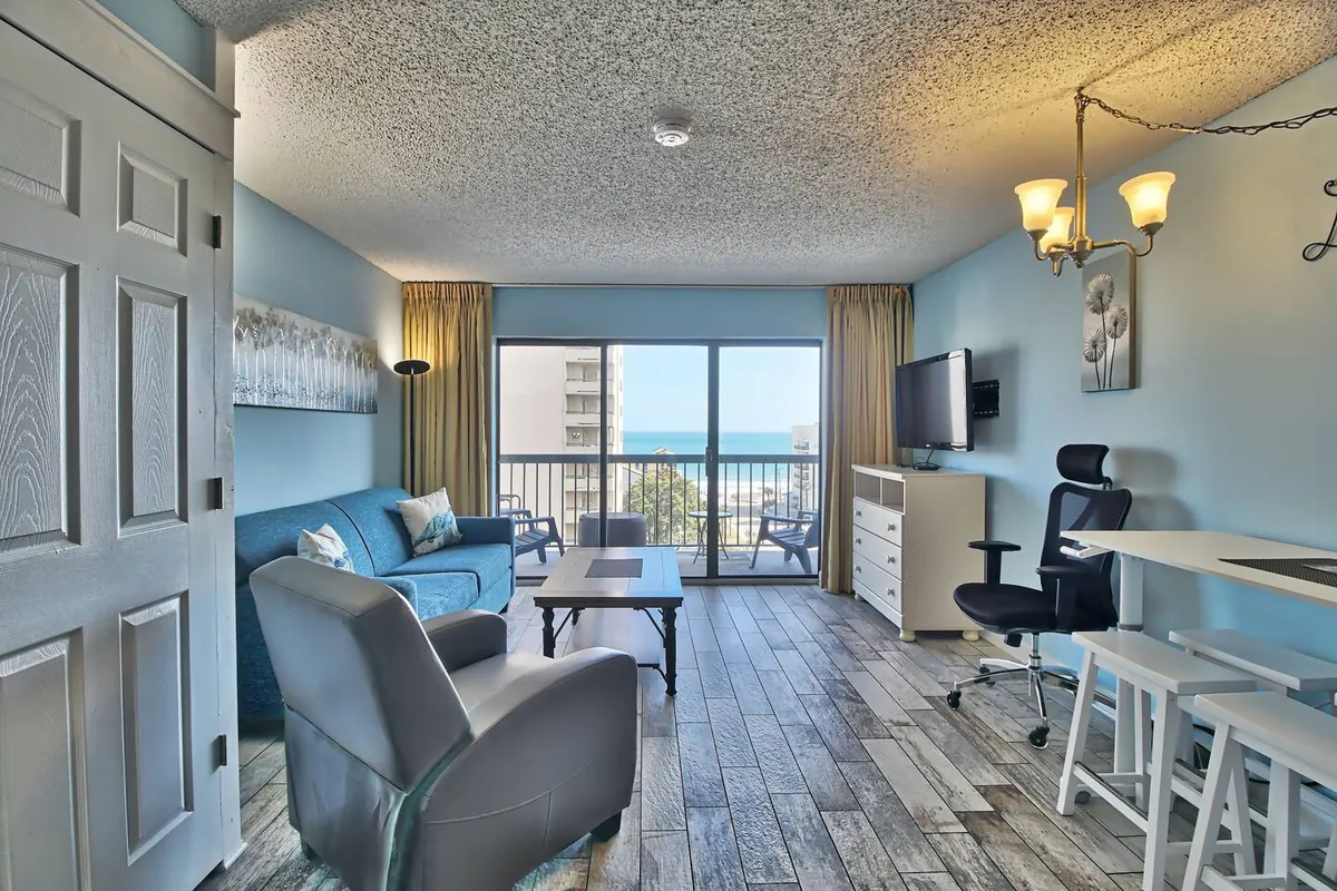 A comfortable seating area opens onto a balcony with a stunning ocean view, framed by modern decor and tranquil touches. The inviting setup is ideal for relaxing with friends or enjoying a quiet moment after a round of golf.