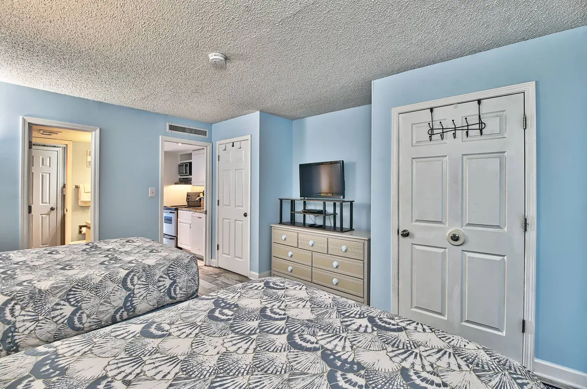 A comfortable bedroom with two beds featuring patterned bedding, a television on a stand, and a dresser with ample drawers for storage. The space is inviting, ideal for families or groups, and offers practical amenities for extended stays.