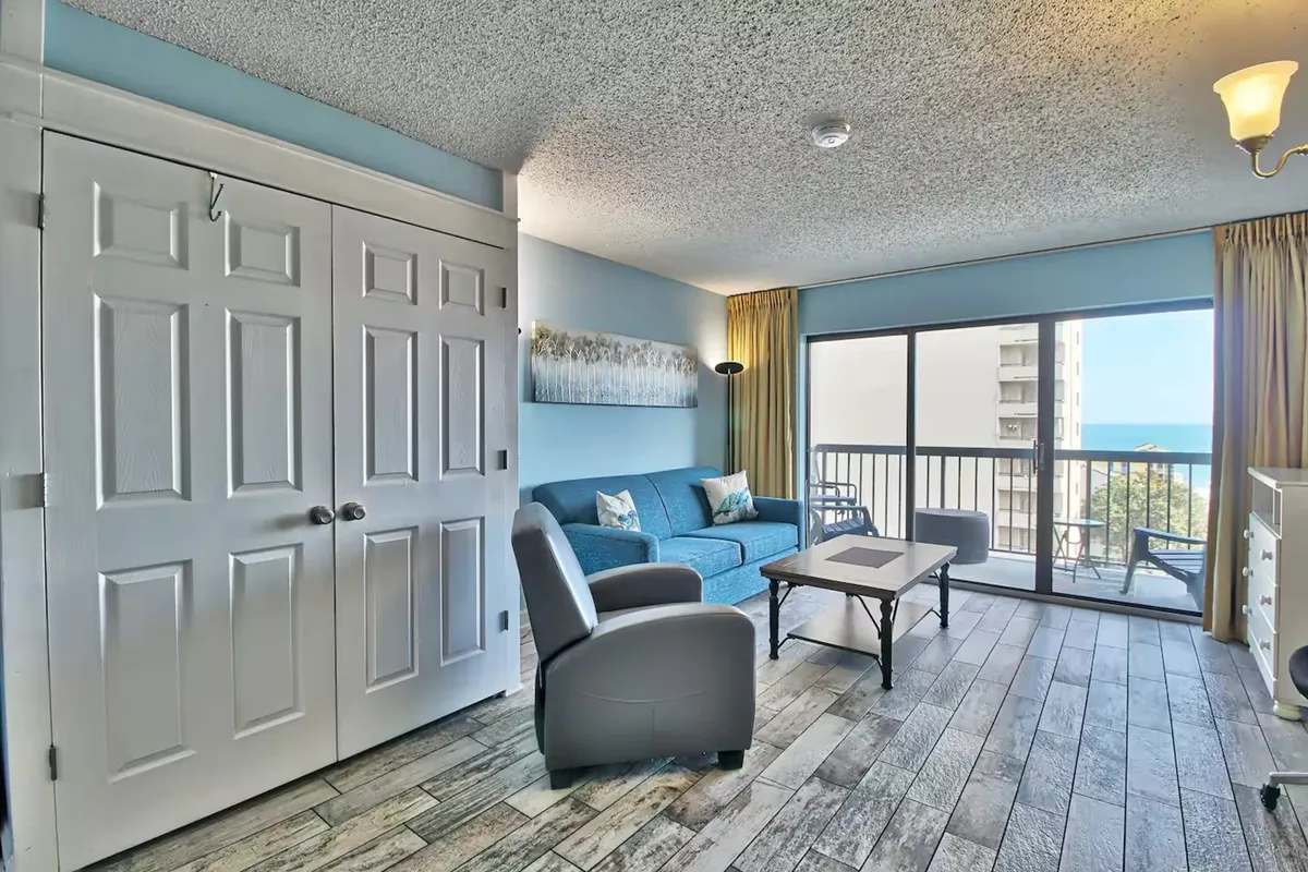 This inviting interior showcases a cozy living space with a comfortable sofa and coffee table positioned before a large window. The window reveals stunning, unobstructed ocean views, allowing in natural light and the tranquil sight of the waves. The space is perfect for gathering with loved ones, relaxing, and soaking up the coastal ambiance.
