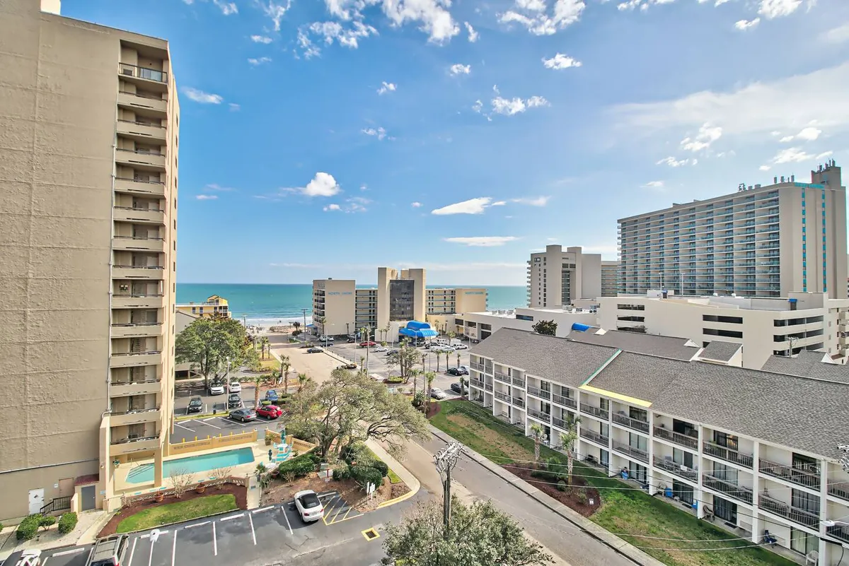 This image offers a sweeping view of the beach, high-rise buildings, a pool area, and a road leading directly to the sand. The photo captures the vibrant seaside atmosphere and the proximity to both water activities and local attractions.