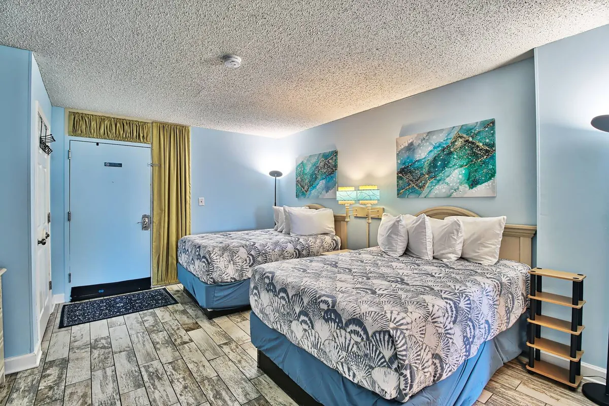 A tranquil bedroom featuring two beds with decorative bedding, colorful wall art above the headboards, and soft-glow nightstands. The entrance door, adorned with a curtain, adds privacy and comfort.