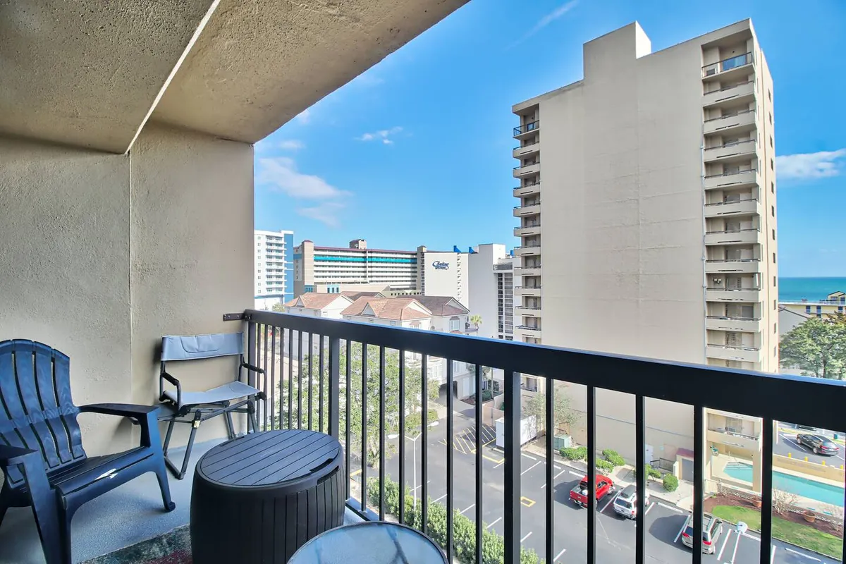 A tranquil exterior shot from the condo’s balcony, featuring outdoor chairs, the balcony railing, and a stunning view of buildings and the ocean. The angle emphasizes the experience of returning home to unwind after a day out.