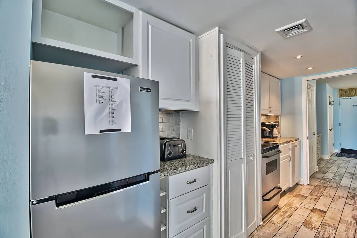 A cozy kitchen scene with a focus on a stainless steel refrigerator, granite countertop, white cabinetry, and a stylish tile backsplash. The space feels open and welcoming, ideal for meal preparation and socializing. The cabinetry and counter space further underscore storage and utility.